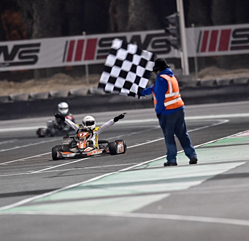 Talal Beshara raising both arms as he takes the chequered flag in his kart