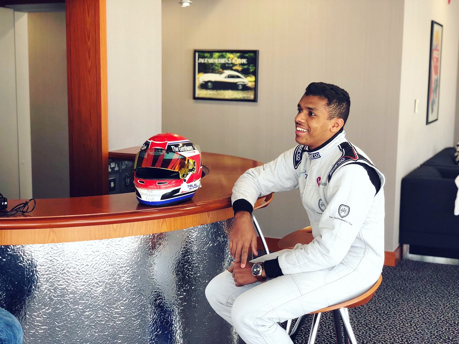 Talal Beshara smiling in his white race suit next to his helmet
